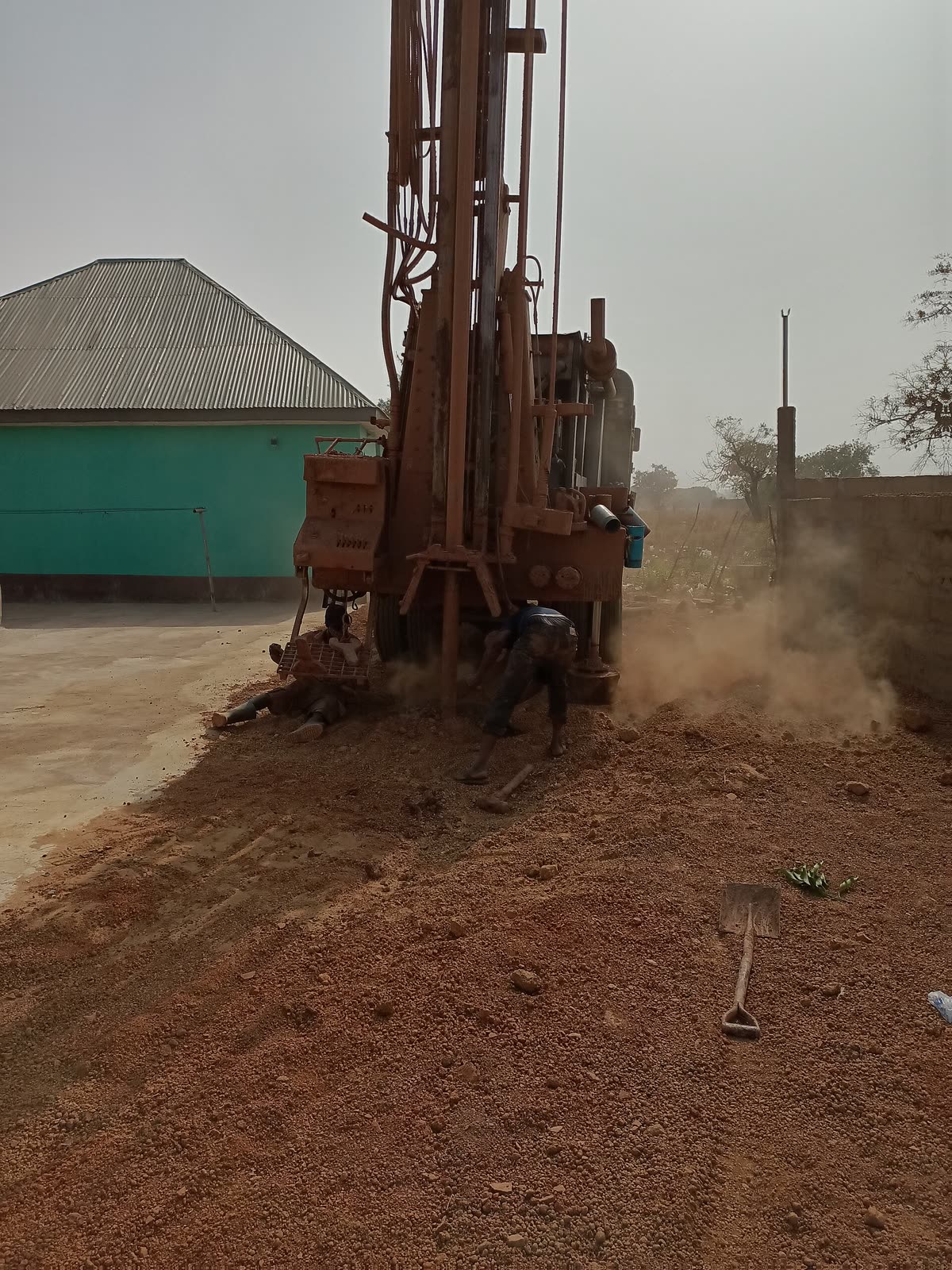 Perfuratriz enferrujada levantando poeira num terreno de terra vermelha